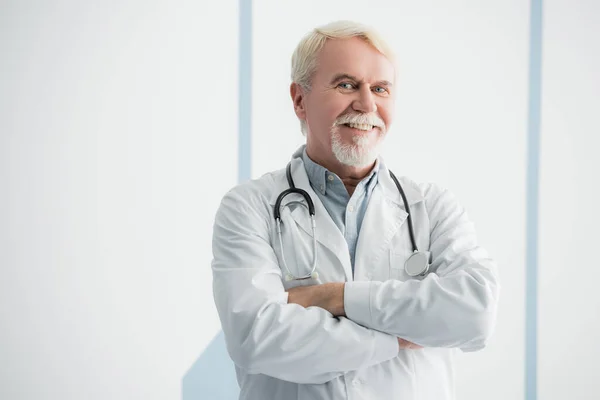 Elderly doctor with crossed arms looking at camera — Stock Photo
