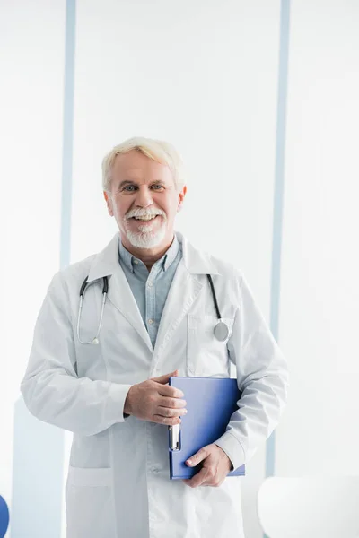 Médico senior sujetando portapapeles mientras trabaja en la clínica - foto de stock