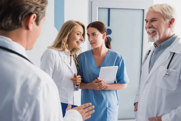 Selective focus of doctor talking to nurse with digital tablet near colleagues in clinic — Stock Photo