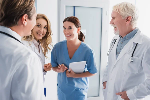 Селективный фокус медсестры с цифровым планшетом, стоящим рядом с врачами в клинике — стоковое фото