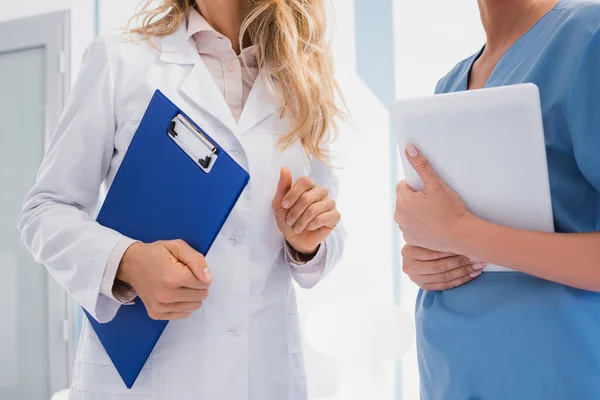 Vista recortada del médico sujetando el portapapeles cerca de la enfermera con tableta digital en la clínica - foto de stock