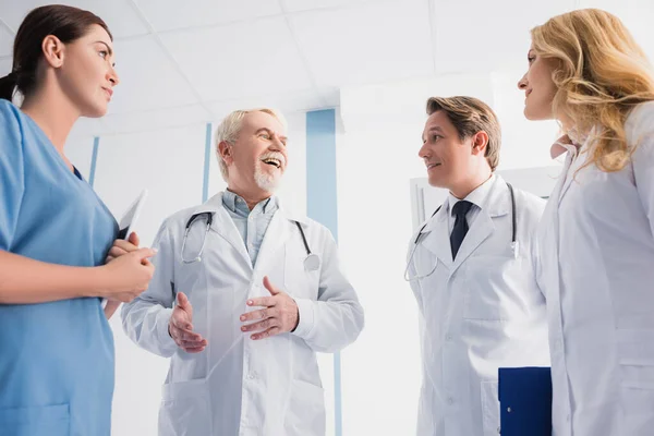 Selective focus of doctors and nurse with digital tablet looking at colleague while talking in hospital — Stock Photo