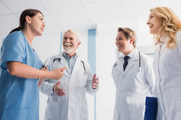 Selective focus of doctors looking at nurse with digital tablet while talking in clinic — Stock Photo