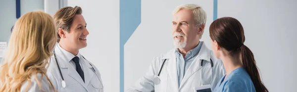 Panoramic crop of doctors and nurse with digital tablet looking at colleague during conversation in clinic — Stock Photo