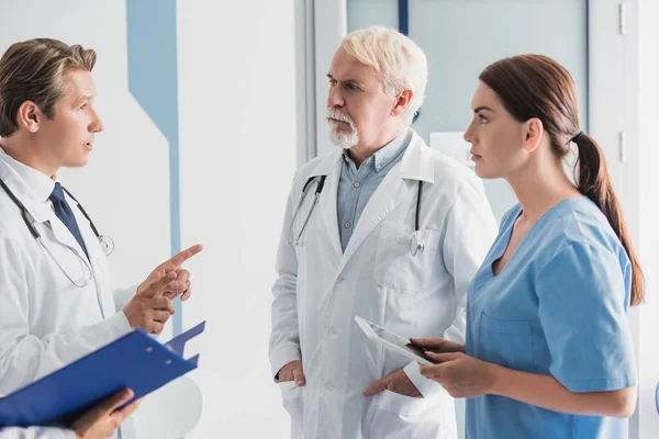 Enfoque selectivo del médico apuntando con los dedos cerca de colegas y enfermera con tableta digital en el hospital - foto de stock