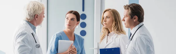 Foto panorámica de médicos y enfermeras con tableta digital mirando a un colega senior en la clínica - foto de stock
