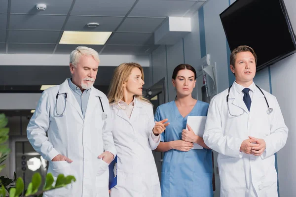 Селективный фокус врача с планшетом, указывающим пальцем на медсестру с цифровым планшетом и коллег в клинике — стоковое фото
