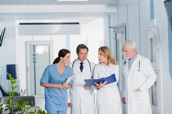 Selective focus of doctor showing clipboard to colleagues and nurse with digital tablet in hospital — Stock Photo