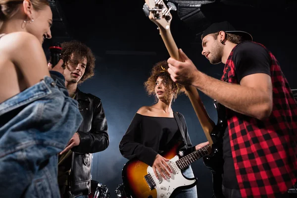 KYIV, UKRAINE - AUGUST 25, 2020: Low angle view of rock band musicians with microphone and electric guitars looking at each other, while talking on black — Stock Photo