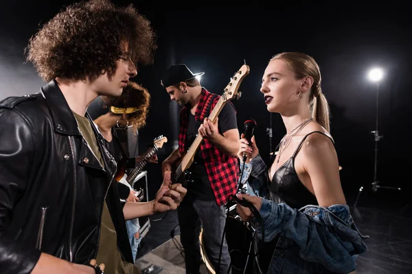 KYIV, UKRAINE - AUGUST 25, 2020: Rock band musician and blonde woman with microphone talking near guitarists with backlit on background — Stock Photo