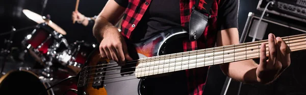 KYIV, UKRAINE - AUGUST 25, 2020: Cropped view of musician playing bass guitar with blurred drummer on background, banner — Stock Photo