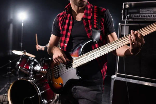 KYIV, UKRAINE - AUGUST 25, 2020: Cropped view of musician playing bass guitar with blurred drummer on background, banner — Stock Photo