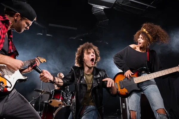 KYIV, UKRAINE - 25 de agosto de 2020: Vocalista encaracolado com boca aberta segurando microfone perto de cordas de guitarra durante a performance da banda de rock em preto — Fotografia de Stock