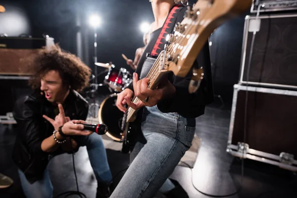 KYIV, UKRAINE - 25 de agosto de 2020: Vocalista entusiasmado com sinal de rock segurando microfone perto de cordas de guitarra com retroiluminação em fundo embaçado — Fotografia de Stock