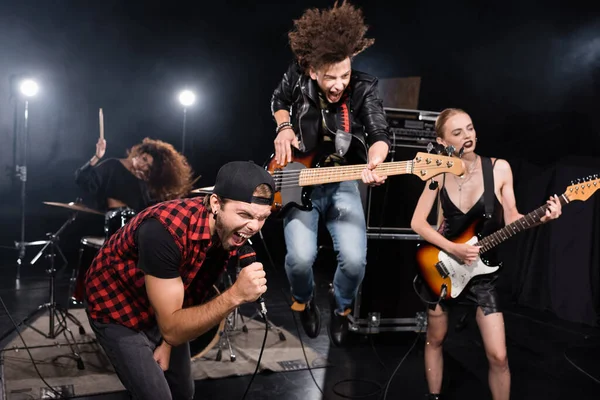 KIEW, UKRAINE - 25. AUGUST 2020: Sänger brüllt in Mikrofon, während er sich nach vorne lehnt und neben Gitarrist aufspringt, während Rockband-Show auf verschwommenem Hintergrund — Stockfoto