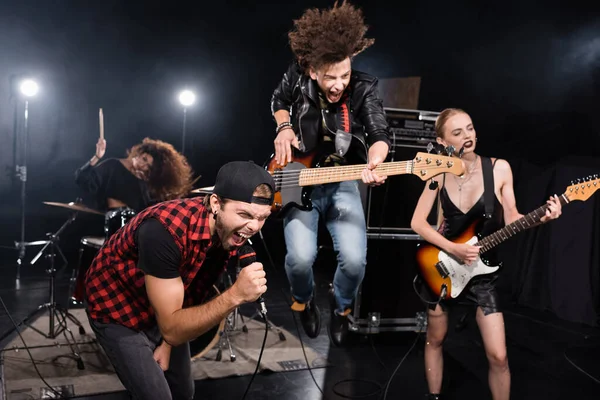 KYIV, UKRAINE - AUGUST 25, 2020: Vocalist shouting in microphone while leaning forward near guitarist jumping up during rock band show on blurred background — Stock Photo