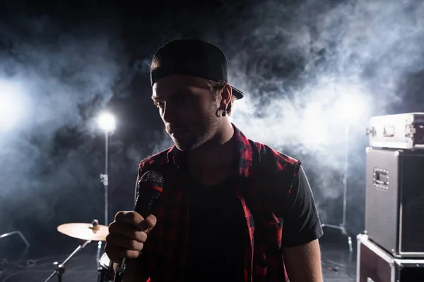 Vocalista de banda de rock sosteniendo micrófono, con humo y retroiluminado sobre fondo borroso - foto de stock