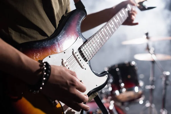 KYIV, UCRANIA - 25 de agosto de 2020: Vista recortada del guitarrista de la banda de rock sosteniendo la selección de guitarra cerca de cuerdas sobre un fondo borroso - foto de stock