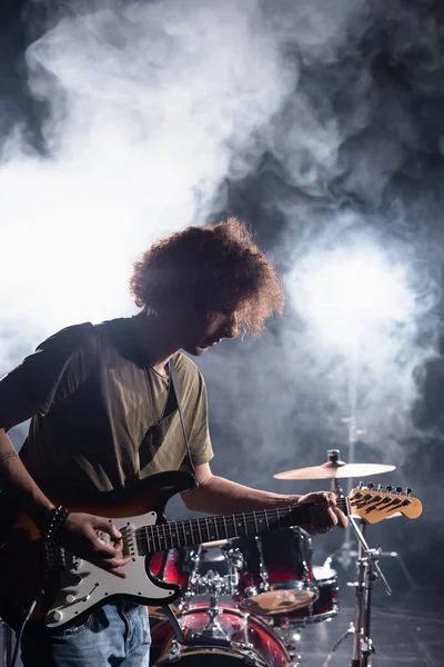 KYIV, UCRAINA - 25 AGOSTO 2020: musicista rock band che suona la chitarra con pick near drum kit con fumo sullo sfondo — Foto stock