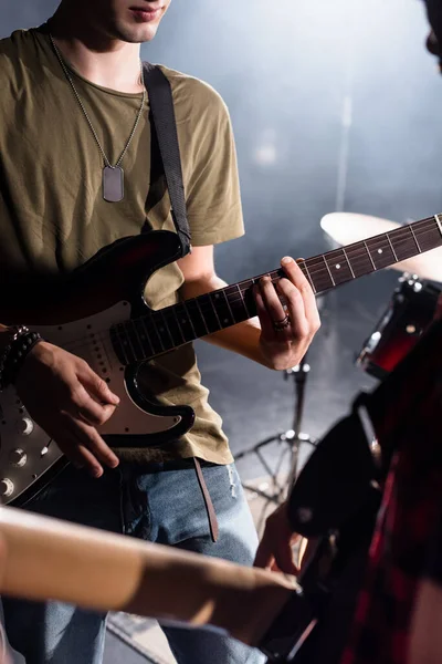 KYIV, UCRANIA - 25 de agosto de 2020: Vista recortada del músico de la banda de rock tocando el bajo con pick con guitarrista borroso en primer plano - foto de stock