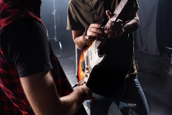 KYIV, UCRANIA - 25 de agosto de 2020: Vista recortada del hombre tocando la guitarra durante el ensayo de la banda de rock con un músico borroso en primer plano - foto de stock