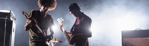 KYIV, UCRANIA - 25 de agosto de 2020: Músicos tocando el bajo con humo y retroiluminados en el fondo, pancarta - foto de stock