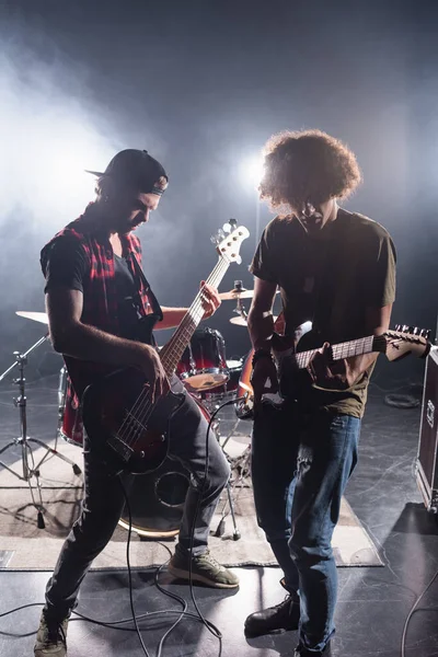 KYIV, UCRAINA - 25 AGOSTO 2020: musicisti rock band che suonano chitarre elettriche vicino alla batteria con retroilluminazione sullo sfondo — Foto stock