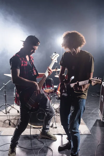 KYIV, UKRAINE - 25 AOÛT 2020 : musiciens de groupes de rock jouant de la guitare électrique près du kit batterie avec contre-jour en arrière-plan — Photo de stock