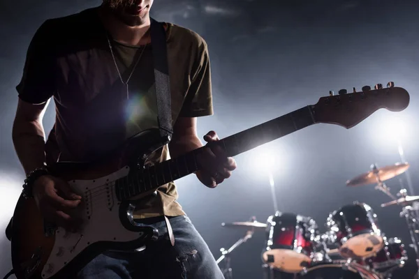 KYIV, UKRAINE - 25 AOÛT 2020 : Vue recadrée d'un musicien d'un groupe de rock jouant de la guitare électrique avec un kit de batterie flou sur fond — Photo de stock