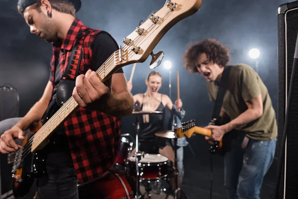 KIEW, UKRAINE - 25. AUGUST 2020: Ernsthafter Musiker spielt E-Gitarre mit hinterleuchteten und verschwommenen Rockband-Mitgliedern im Hintergrund — Stockfoto