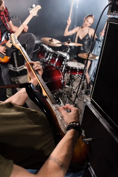 KYIV, UCRANIA - 25 de agosto de 2020: Hombre con pico tocando el bajo cerca del amplificador combinado con la mujer rubia tocando la batería ang guitarrista sobre fondo borroso - foto de stock