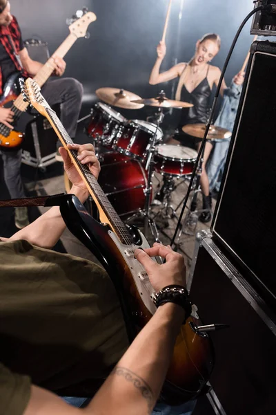 KYIV, UKRAINE - AUGUST 25, 2020: Man with pick playing bass guitar near combo amplifier with blonde woman playing drums ang guitarist on blurred background — Stock Photo