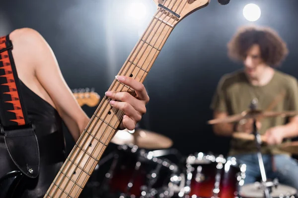 Close-up vista de músico feminino tocando guitarra elétrica com baterista desfocado e kit de bateria no fundo — Fotografia de Stock