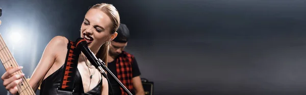 Vocalista da banda de rock com guitarra elétrica cantando em microfone com homem retroiluminado e borrado no fundo, banner — Fotografia de Stock