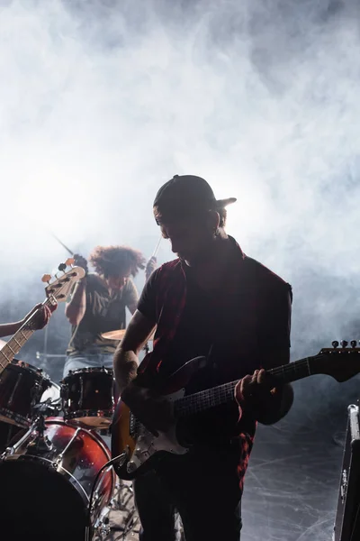 KYIV, UKRAINE - AUGUST 25, 2020: Rock band member playing guitar with blurred drummer and drum kit on background — Stock Photo