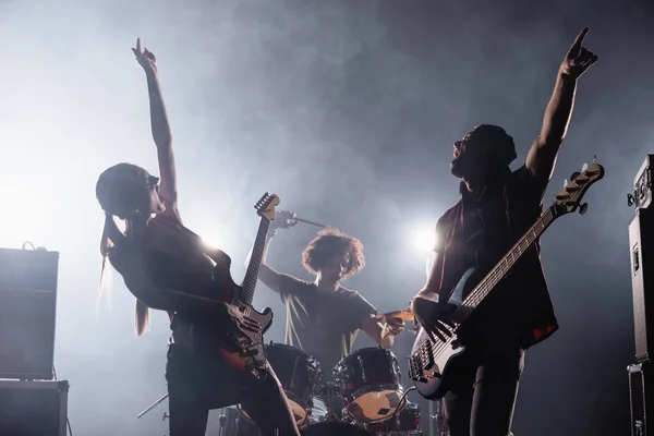 KYIV, UCRANIA - 25 de agosto de 2020: guitarristas de la banda de rock con las manos en el aire cantando con humo y batería en el fondo - foto de stock