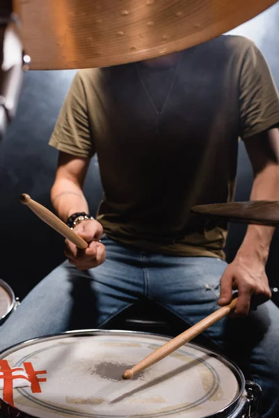 Неясное лицо музыканта с барабанными палочками, играющего на черном барабане — стоковое фото