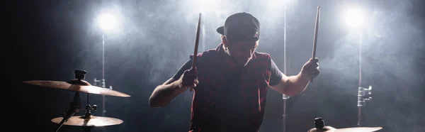 Miembro de la banda de rock con baquetas tocando la batería con retroiluminación y humo en el fondo, pancarta — Stock Photo