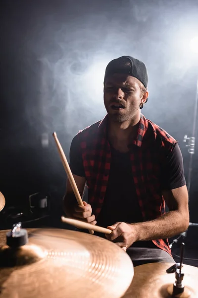 Rockband-Musiker hält Drumsticks in der Hand und spielt auf Trommeln mit Rauch auf schwarz — Stockfoto