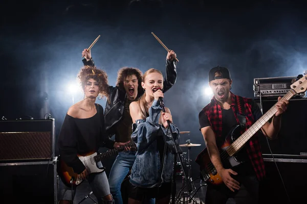 KYIV, UKRAINE - AGOSTO 25, 2020: Músicos da banda de rock gritando enquanto seguram instrumentos musicais com retroiluminação em preto — Fotografia de Stock