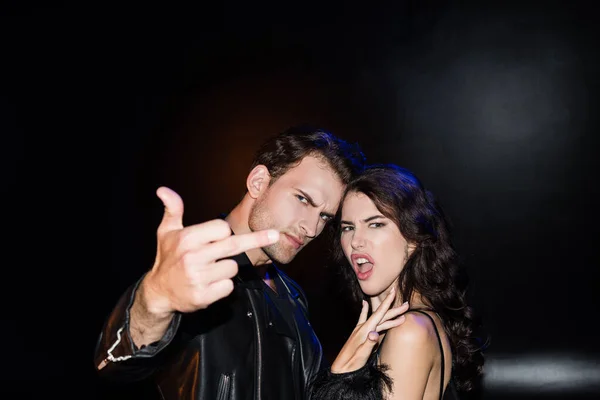 Angry man showing middle finger, standing near brunette woman gesturing on black on blurred foreground — Stock Photo