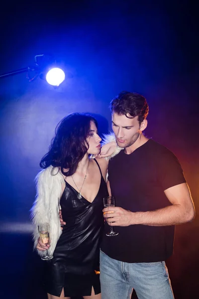 Donna bruna riccia con bicchiere di champagne appoggiato sul fidanzato in camicia con retroilluminazione su nero — Foto stock