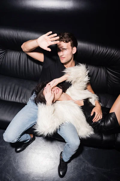 Высокий угол зрения сексуальной пары, закрывающей глаза и лицо руками, сидя на диване в ночном клубе — стоковое фото
