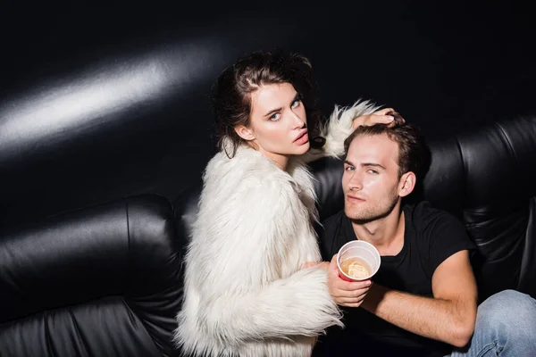 Mujer en chaqueta blanca tocando el pelo novio mirando a la cámara en discoteca - foto de stock