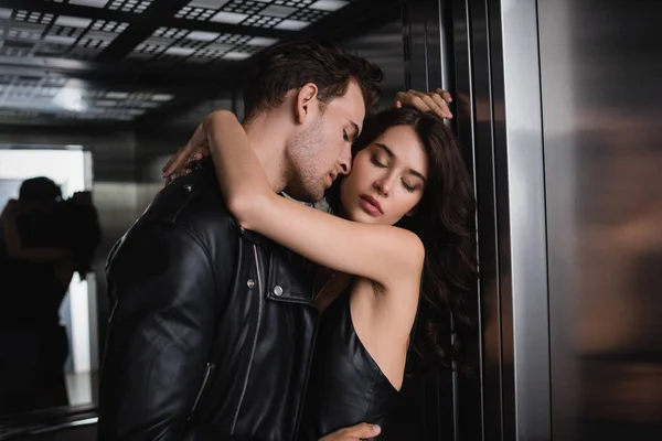 Homem apaixonado em casaco preto abraçando mulher sexy com olhos fechados no elevador — Fotografia de Stock