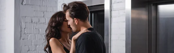 Sensual brunette woman with closed eyes touching man in black t-shirt near elevators, banner — Stock Photo