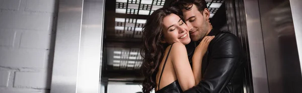 Feliz pareja de jóvenes adultos con los ojos cerrados abrazándose en la entrada del ascensor, pancarta - foto de stock