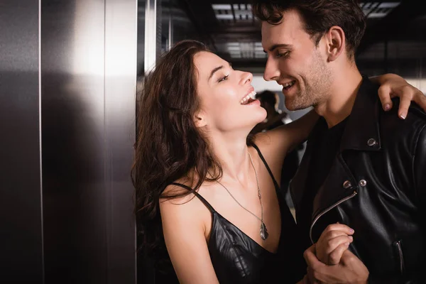 Брюнетка смеется, обнимаясь и глядя на улыбающегося мужчину в кожаной куртке в лифте — стоковое фото