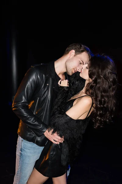 Homem apaixonado em jaqueta de couro dobrando e olhando para os lábios de mulher encaracolada em preto — Fotografia de Stock