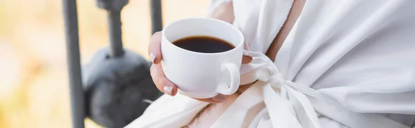 Abgeschnittene Ansicht einer Frau im weißen Gewand, die Kaffee auf dem Balkon trinkt, horizontales Banner — Stockfoto